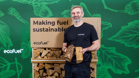 ECOFUEL™ team member holding kiln-dried hardwood logs in front of sustainable firewood packaging.