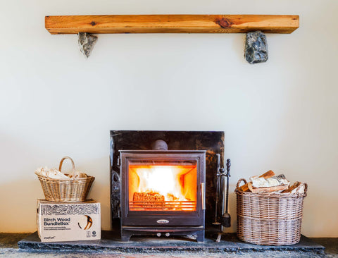 Wood-burning stove lit in daylight beside stacked ECOFUEL Birch firewood during early spring in Ireland