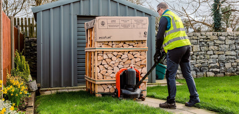 ECOFUEL™ delivery driver moving a DoubleDeck® kiln-dried firewood crate beside a storage shed