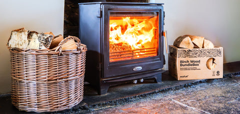 ECOFUEL™ kiln-dried Birch firewood in 25L BundleBox® sits beside a lit wood-burning stove and the basket of Birch logs.