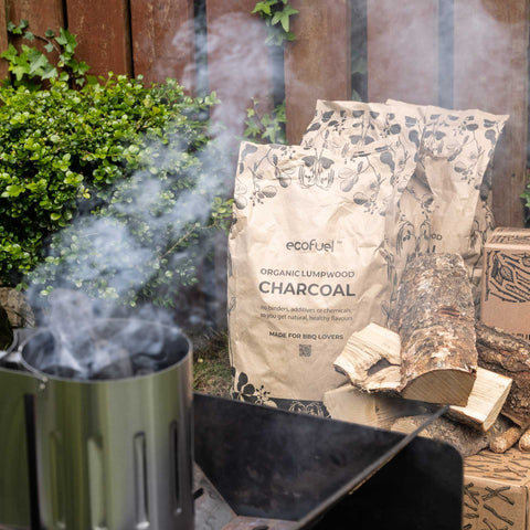 Eco-friendly BBQ setup with ECOFUEL™ Organic Lumpwood Charcoal, chimney starter, and firewood in a garden scene