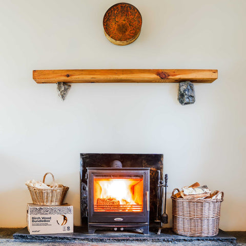 Wood-burning stove with baskets of firewood and an Ecofuel Birch Bundle box on a stone hearth.