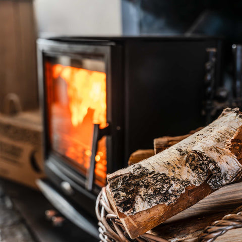 Wood stove with burning fire and a basket of Ecofuel kiln -dried Birch logs in front