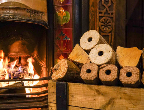 ECOFUEL™ firewood logs and wood briquettes stacked against a fireplace with flames inside
