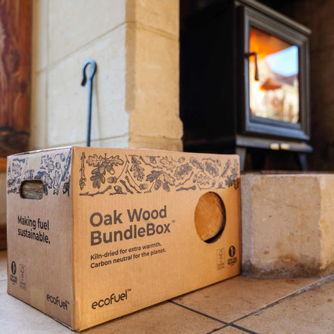 Cardboard box labeled 'Oak Wood BundleBox' by ecofuel in front of a wood-burning stove.