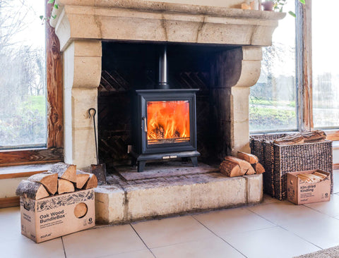 Wood-burning stove lit in daylight beside stacked Ecofuel Oakwood BundleBox firewood during early spring in Ireland