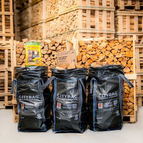 Three black bags labelled 'CityBag' are in front of stacked firewood in a warehouse.